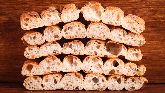 A closeup shot of half-sliced barbari bread pieces piled up against the brown wooden wall background