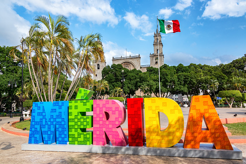 Merida, Mexico – April 21, 2017: MERIDA, MEXICO - FEBRUARY 21: Colorful Merida sign with a Mexican flag and cathedral in the background in Merida, Mexico on February 21, 2017