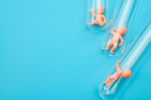 Artificial insemination, IVF and in vitro fertilization concept with babies in test tubes with each baby in a different test tube isolated on blue background with copy space