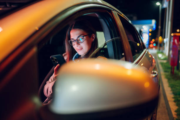 Business woman driving a car in a city during a night and using smartphone Portrait of a beautiful business woman using smartphone in a car at night. Busy female working on a mobile phone while sitting on a driver seat. Bokeh and neon city lights in the background. car city urban scene commuter stock pictures, royalty-free photos & images