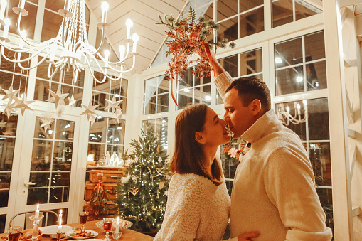 Midnight kiss. Young happy family couple in love kissing and hugging during New Years Eve celebration at cozy festively decorated room with xmas tree and festive dinner table