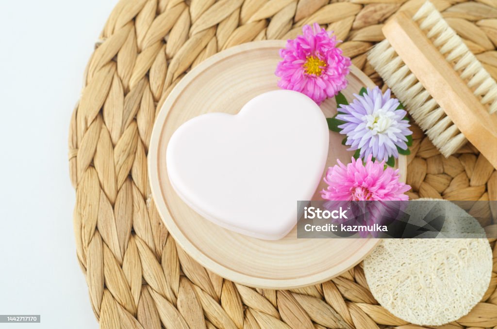 Heart shaped bar of soap (facial cleanser, solid shampoo) and purple flowers. Natural beauty treatment and skin care concept. Top view, copy space. Bar Of Soap Stock Photo