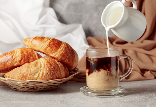 Freshly baked croissants and coffee with cream. Pouring creme in a glass cup of coffee.