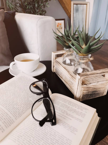 Eyeglasses on open book lying on round coffee table decorated with aloe plants