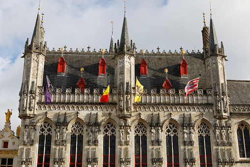 Bruges, Belgium - September 10, 2022: Upper fragment of decorative facade and a roof with turrets of Bruges City Hall which is located on Burg Square in the centre of the city
