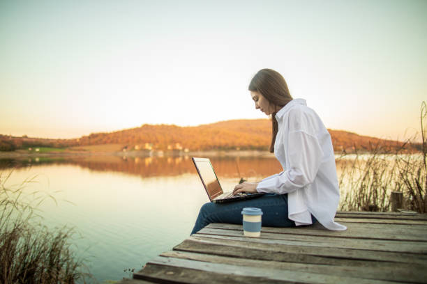 istock Young beautiful woman using laptop outside by lake 1442730167