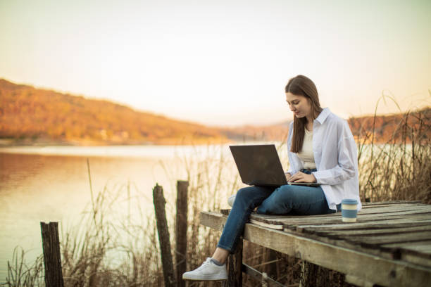 istock Young beautiful woman using laptop outside by lake 1442730169