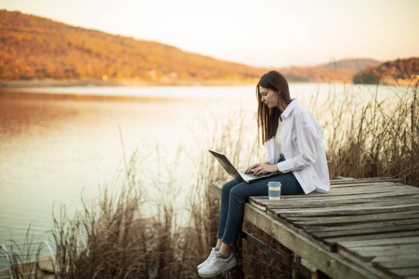 istock Young beautiful woman using laptop outside by lake 1442730170
