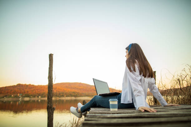istock Young beautiful woman using laptop outside by lake 1442730226