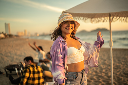 Portrait of young woman at the beach with friends on social gathering on background