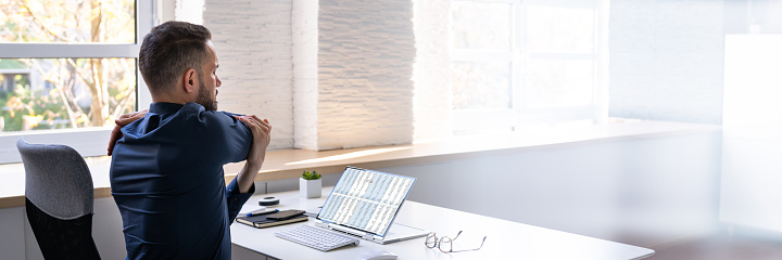 Employee Stretching At Office Desk At Work