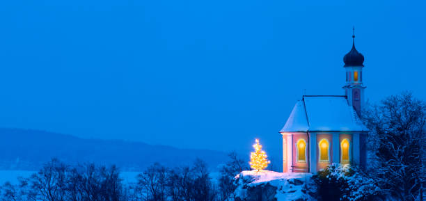 romantica cappella natalizia illuminata con albero di natale davanti al cielo blu e fuochi d'artificio multicolori - snow chapel christmas germany foto e immagini stock