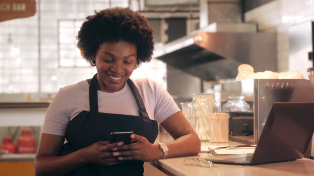 One African American female startup barista stands at casual ,Using a smartphone