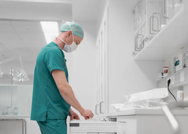istock Man in uniform picking up instruments from drawer in operating room 1442734550