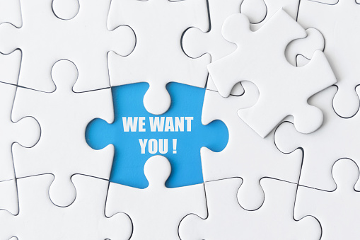 Job posting concept: White puzzle with one missing piece shows: WE WANT YOU!