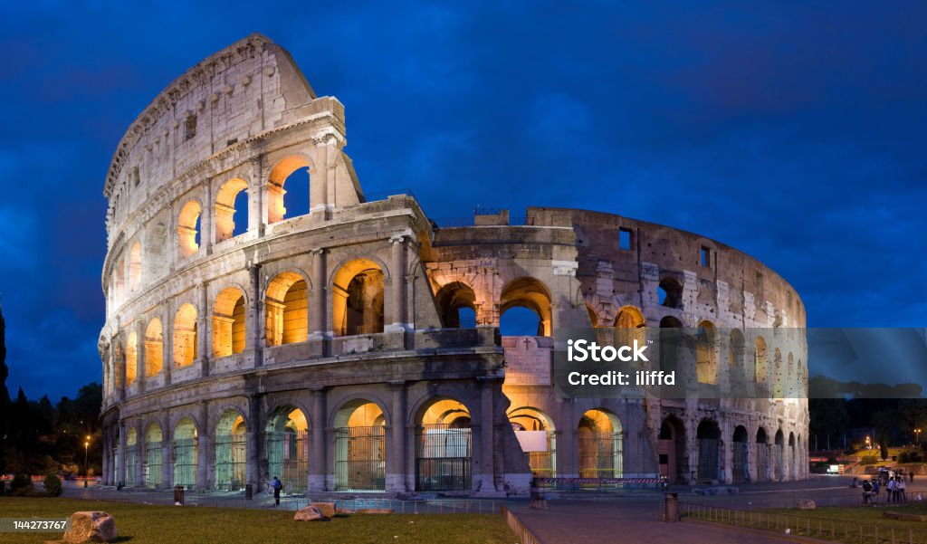 The magnificent Colosseum at dusk in Rome The Colosseum in Rome, Italy, lit at dusk.  The building, which is lit inside and out, is set against a dark blue sky with soft clouds. Blue Stock Photo