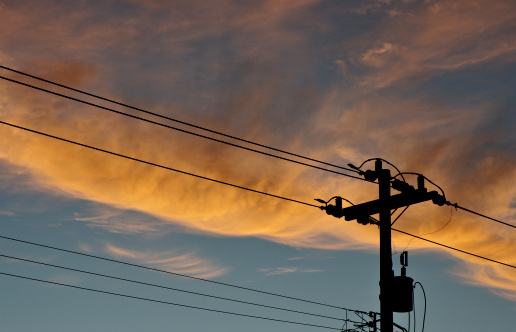 A silhouette of a telephone pole and powerlines with a backdrop of clouds at dusk.