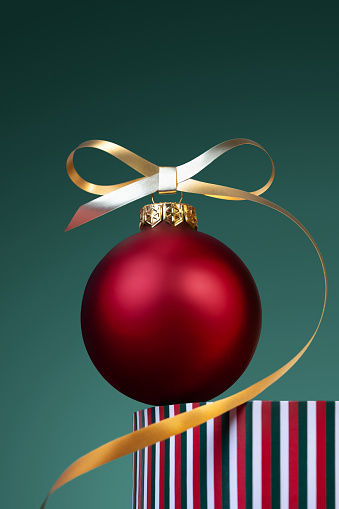 A red Christmas bauble with a golden ribbon bow on a striped pedestal. Christmas scene. Bright Christmas ball on a green gradient background.