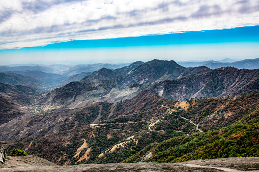 A scenic view of the western side of the Sierra Nevada mountains seen from Moro Rock in Sequoia National Park. An unusual cloud layer is in the sky and smog is visible over the San Joaquin Valley.