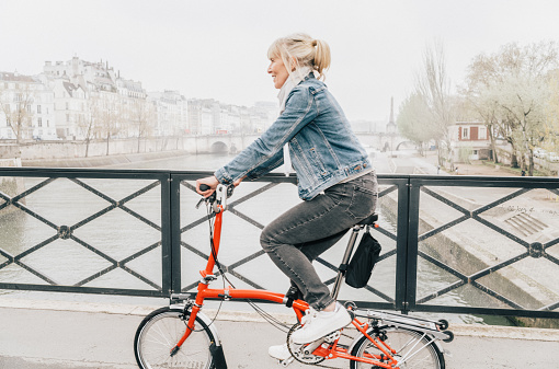 Mature woman cycling on the Pont de l'Archeveche over the River Seine on a cloudy, foggy spring day in Paris.