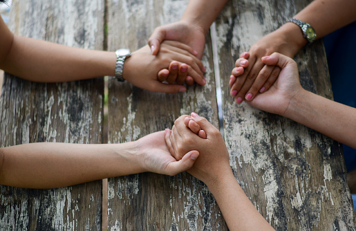 Group of people Praying Hands Over The Bible On Wooden Desk