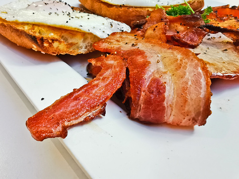 Big bacon in English breakfast with sunny fried eggs, bacon, tomatos, ham on Turkish flat grilled bread on white dish