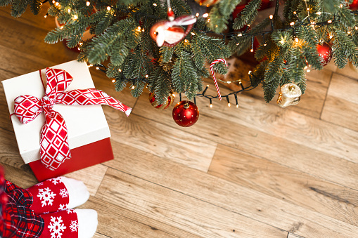 Christmas tree decorated in red, white and green with gifts against a large picture window and a wintery outdoor scene.