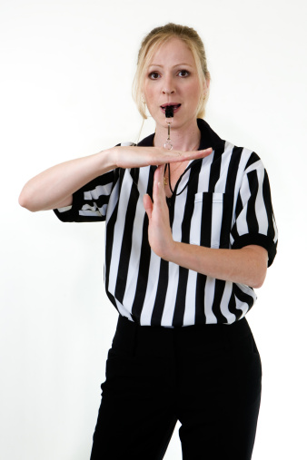 Attractive blonde woman wearing black and white striped referee uniform blowing on a whistle making the hand signal for technical foul or time out