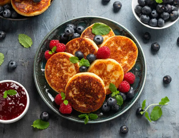 Cottage cheese pancakes served with blueberries, raspberries, strawberry jam and mint leaves, healthy vegetarian protein breakfast.