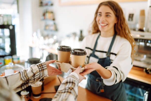 uśmiechnięta baristka - dziewczyna rozdająca kubki kawy na wynos klientowi. - barista zdjęcia i obrazy z banku zdjęć