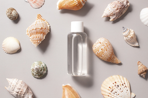 Cosmetic bottle with tonic water with seashells. The concept of a summer cosmetic moisturizing serum with collagen and organic sea minerals.