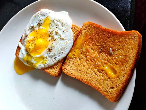 Overhead view of 2 slices of toasted crusty bread, with a fried sunny side up egg placed on top. Perfect for Breakfast, lunch, or a light dinner.