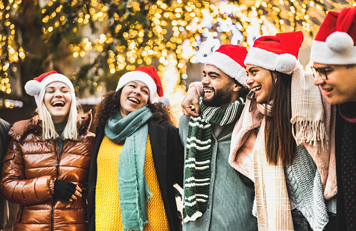 Trendy people group walking under Christmas tree decoration - Winter life style concept with happy friends wearing red santa hats while having fun holidays together outside - Warm lights bright filter