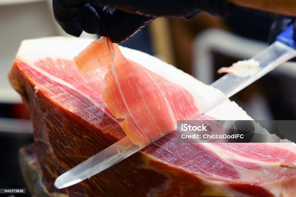 hand of the butcher who with a sharp knife slices a slice of raw ham gloved hand of the butcher who with a sharp knife slices a slice of raw ham Butcher's Shop Stock Photo