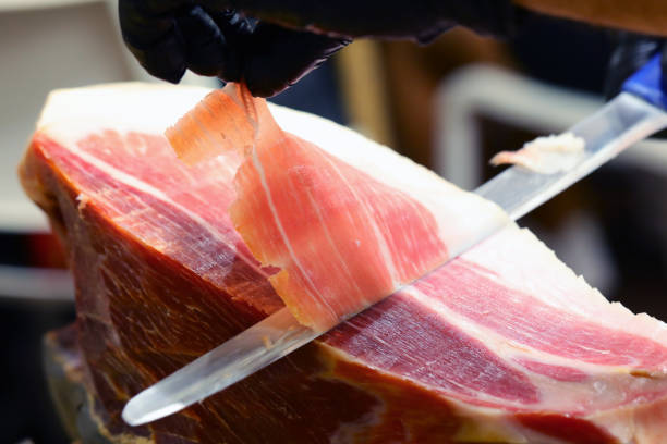 hand of the butcher who with a sharp knife slices a slice of raw ham gloved hand of the butcher who with a sharp knife slices a slice of raw ham prosciutto stock pictures, royalty-free photos & images