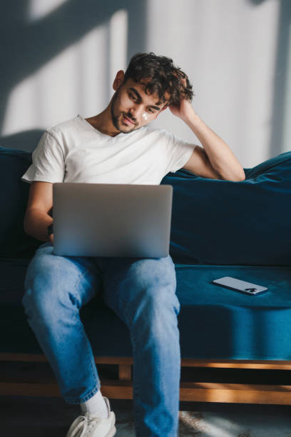 istock Relaxed young man working on laptop pc computer sitting on blue sofa, spending time in living room at home. nternet communication. Modern communication. Internet technology. 1442780067