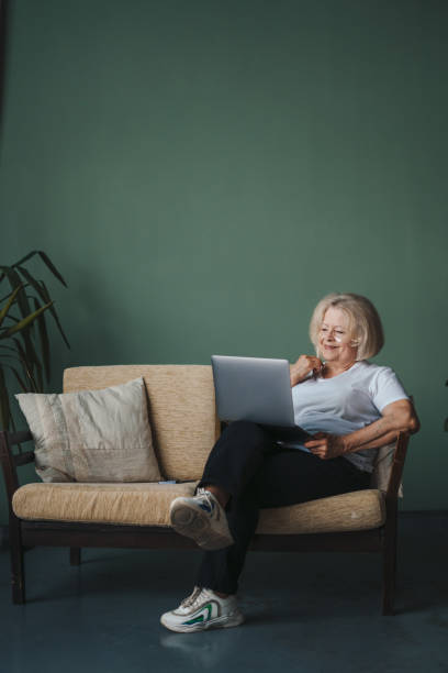 istock Senior woman with under eye patches sitting on the sofa in front of laptop during remote work. Contemporary portrait. Elderly generation online. Beauty portrait. 1442780098
