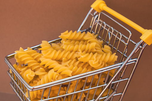 Shopping trolley cart Filled With Pasta on Beige background. Copy space for your text. Food and groceries shopping price increase, Rising food cost food crisis inflation concept. Online shopping, buy mall market shop consumer