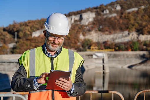 Male engineer working with a digital tablet in hydroelectric dam. Renewable energy systems.