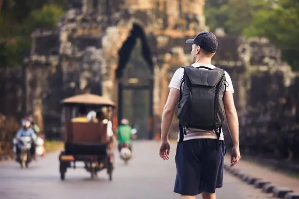 Man with backpack is walking to ancient city. Rear view of tourist, Siem Reap, Cambodia.