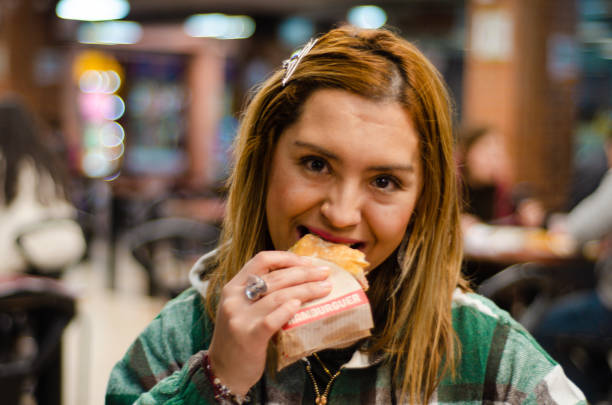 istock Woman smiling and eating a hamburger looking at camera 1442785085