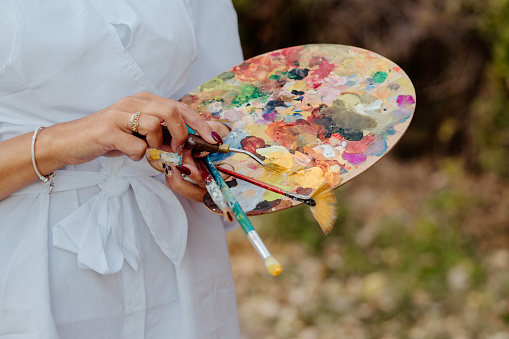 Close up of female painter's hands holding a color palette and paintbrush