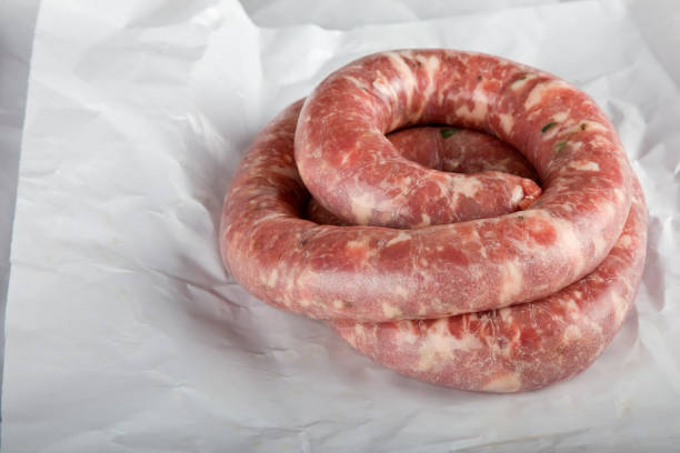 Bunches of freshly prepared raw sausages hanging on wooden background