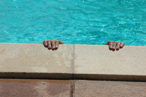 Child's hands on the border of the swimming pool