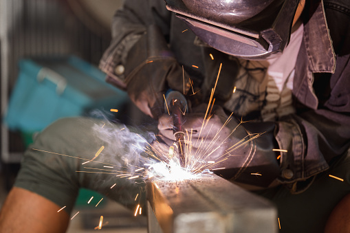 Male worker welding steel, sparks from light, protective masks and gloves increase safety.