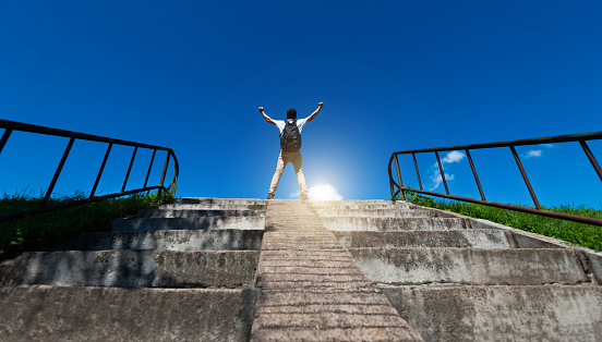 Young man raising hands on top of stairs
