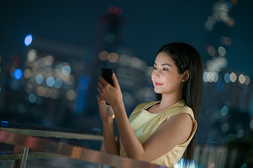 Successful Asian Businesswoman owner using phone checking an e-mail at the Rooftop of luxury hotel at night