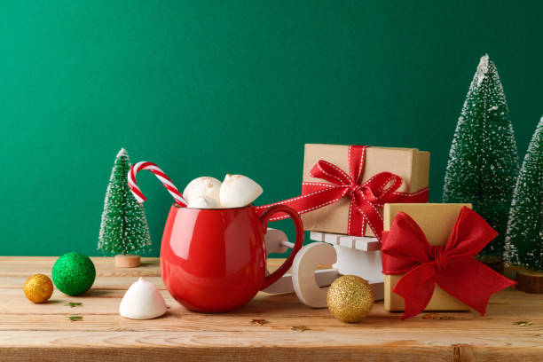istock Christmas hot chocolate cup with marshmallow, gift boxes and decorations on wooden table over green background. Festive greeting card 1442790397