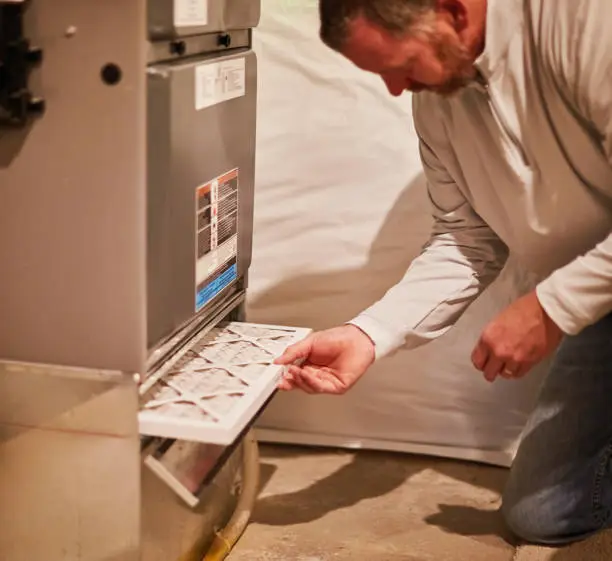 Photo of Male home inspector assessing the heating system in the mechanical room of a residential property