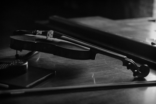 Een viool op een piano in zwart wit. De viool wordt van één kant belicht.